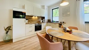 A modern kitchen with white cabinets, a wooden countertop, and a dining area with a round table and pink chairs.