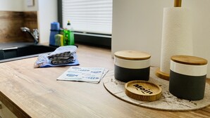 A kitchen counter with a sink, a stack of folded towels, two wooden containers, and a large paper towel roll.