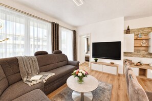 A modern living room with a sofa, a coffee table, a flat-screen TV, and a small dining area.