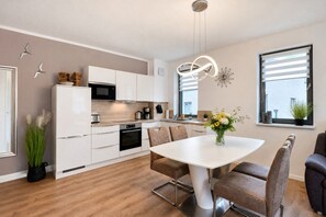 A modern kitchen with white cabinetry, a built-in oven, and a dining area with a white table and brown chairs. - Welcome to the Morgensonne vacation apartment in Parkvillen Baabe (Baabe)