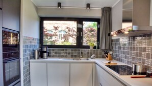 A modern kitchen with white cabinets, a black countertop, a window with a view of a brick building, and a tiled backsplash. - Welcome to the Brick Quarter South Putbus on the island of Rügen (Putbus)