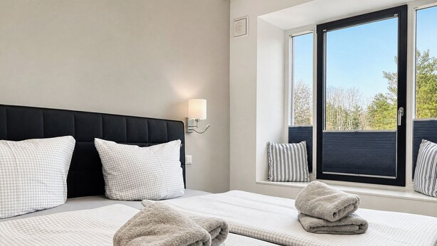 Una camera d'albergo con una grande finestra, un letto con lenzuola a quadretti e una testiera nera.