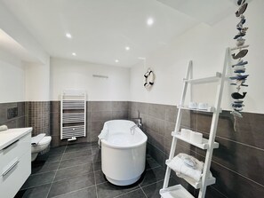 Bathroom features a central bathtub, wall-mounted toilet, and towel rack.