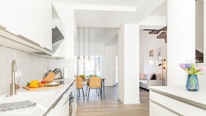 A modern kitchen with white cabinetry, a wooden dining table, and a view into the living area. - Sunshine by the sea: a modern oasis for unforgettable moments in Prora, Rügen (Prora)