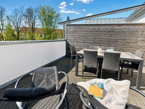 A rooftop terrace with a table and chairs, a covered area, and a view of trees and buildings.