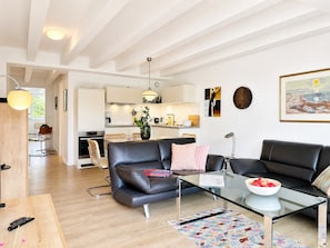 A modern living room with a glass coffee table, leather sofas, and a kitchen in the background.