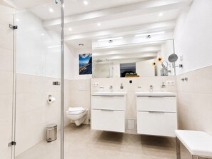 A modern bathroom with a glass shower enclosure, a toilet, and a double sink vanity.