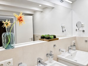 A modern bathroom with two sinks, a mirror, and a vase with flowers on the countertop.