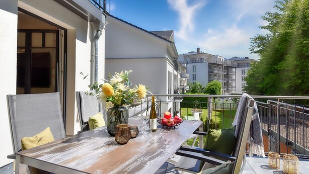 A balcony with a table set for two, featuring a vase with flowers, a bottle, and a bowl of fruit. - Charming "Meereslauschen" vacation apartment in Villa Beatrice: luxury, comfort (Binz)