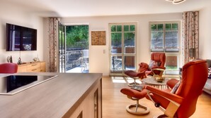 A modern living room with a wooden coffee table, red chairs, a flat-screen TV, and large windows offering a view of the outdoors. - Charming "Meereslauschen" vacation apartment in Villa Beatrice: luxury, comfort (Binz)