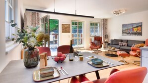 A modern living room with a sofa, a dining table set with plates, and a vase with flowers. - Charming "Meereslauschen" vacation apartment in Villa Beatrice: luxury, comfort (Binz)