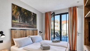 A hotel room with two beds, a large window with curtains, a painting on the wall, and a view of buildings outside. - Relaxed Baltic Sea vacation: vacation apartment Strandperle in Binz with lake view (Binz)