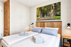 Ett hotellrum med en säng, en sänggavel i trä, en tavla som hänger på väggen och ett nattduksbord med en lampa.