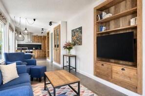 Ett modernt vardagsrum med en soffa, ett soffbord och en platt-TV som är monterad på en väggpanel i trä.
