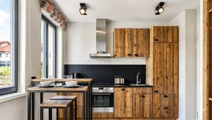 A modern kitchen with wooden cabinets, a stainless steel range, and a dining area with stools. - Relaxed Baltic Sea vacation: vacation apartment Strandperle in Binz with lake view (Binz)