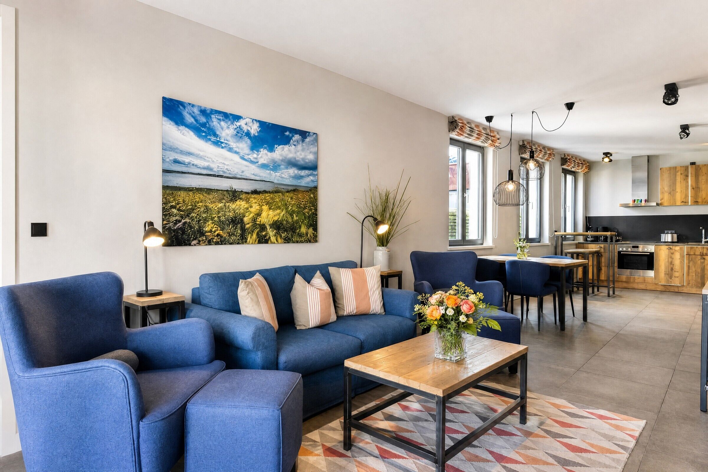 Un salon moderne avec un canapé bleu, une table basse et un tableau représentant un paysage.