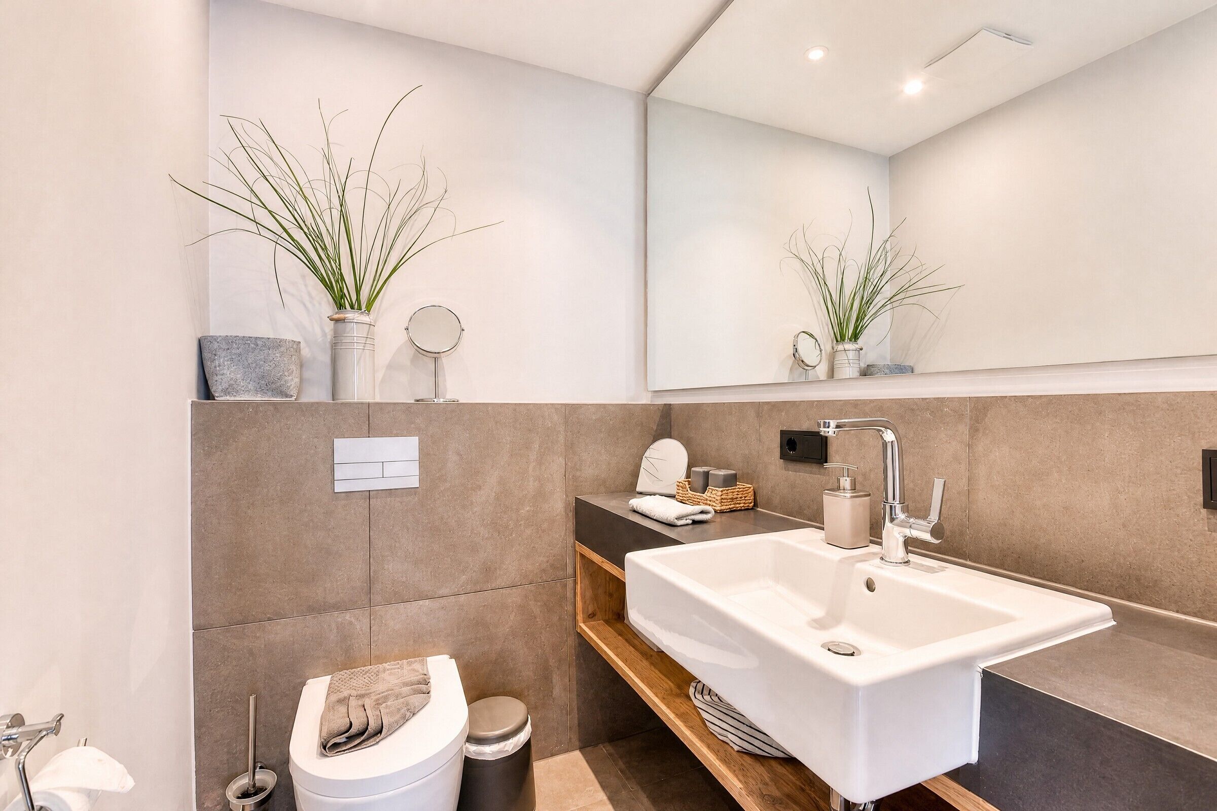Un baño moderno con un espejo grande, un lavabo blanco y un inodoro.
