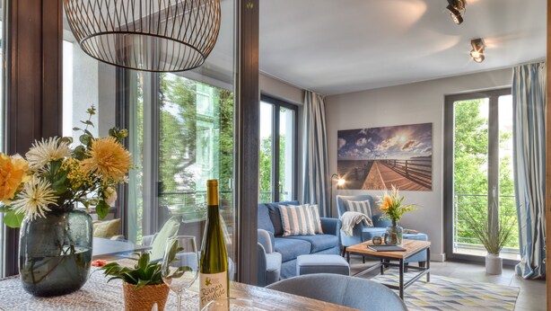 En moderne stue med et stort vindue, en sofa, et sofabord og et spisebord med en vase blomster og en vinflaske.