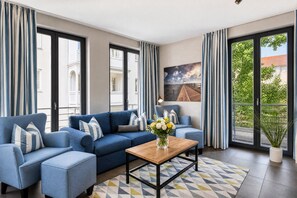A modern living room with a blue sofa set, a wooden coffee table, and a large window with curtains.