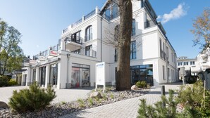 En moderne bygning med en hvid facade, store vinduer og en indgang med brosten.