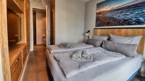 Une chambre à coucher avec un lit, une literie à carreaux, un tableau représentant un coucher de soleil et une tête de lit en bois.