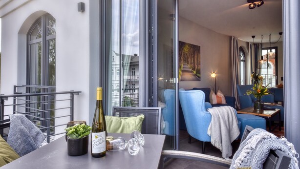Un intérieur moderne avec une cloison en verre, des sièges bleus, une table avec une bouteille et des verres, et une vue sur l’extérieur.