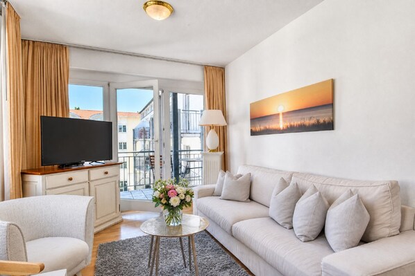 Una sala de estar moderna con un televisor de pantalla plana, un sofá, una mesa de centro y un cuadro de un atardecer.
