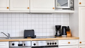 Una cocina con armarios blancos, microondas, tostadora, cafetera y estufa.