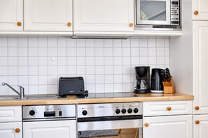 A kitchen with white cabinets, a microwave, a toaster, a coffee maker, and a stove.