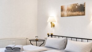 Una habitación de hotel con cama, mesita de noche, lámpara, radiador y un cuadro en la pared.