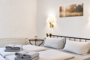 A hotel room with a bed, a bedside table, a lamp, a radiator, and a painting on the wall.