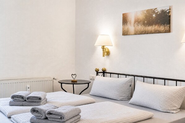 A hotel room with a bed, a bedside table, a lamp, a radiator, and a painting on the wall.