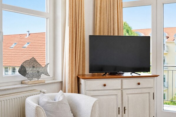 A room with a television on a wooden stand, a white cabinet with drawers, and a window with curtains.