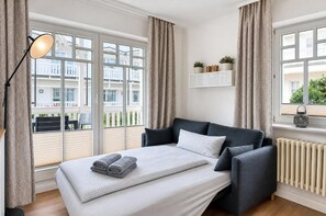 Habitación de hotel con cama, lámpara de noche, ventana con cortinas, radiador y vistas al exterior.