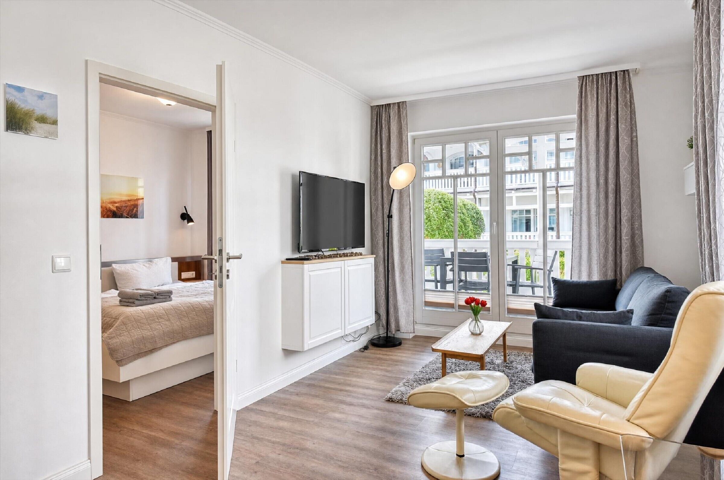 A modern living room with a sofa, a coffee table, a TV, and a bed in the adjacent room.