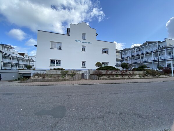A white building with the name "Villa Secadler" on the facade, featuring multiple windows and a gated entrance.