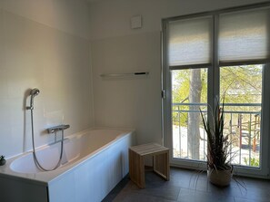 Moderni kylpyhuone, jossa on kylpyamme, suihku ja ikkuna, josta on näkymä ulos.