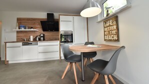 A modern kitchen with white cabinets, a wooden countertop, and a dining area with a wooden table and black chairs.