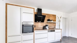 A modern kitchen with white cabinetry, a built-in oven, a black range hood, and a wooden accent wall.