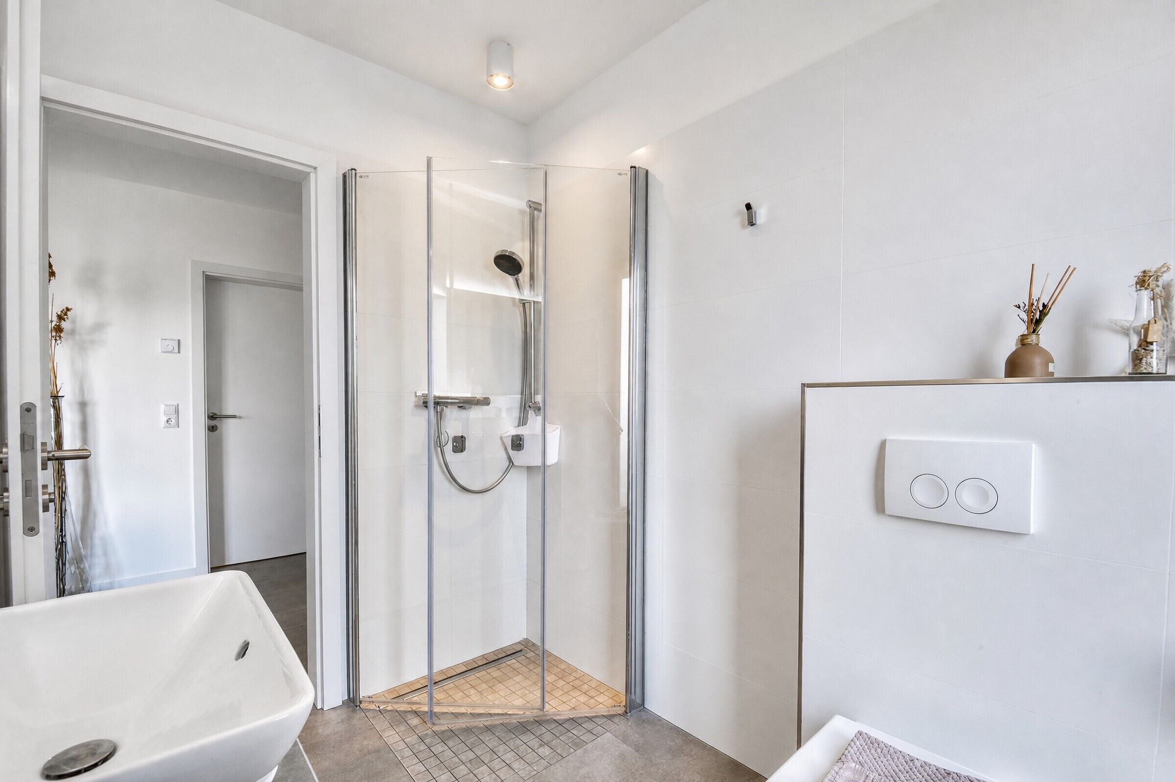 Un bagno moderno con cabina doccia in vetro, una vasca da bagno bianca e un corpo illuminante a parete.