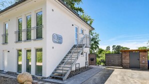 A modern building with a staircase leading to the entrance, a sign indicating 'Quartier Sellin Ostseeg 29 b', and a small outdoor seating area.
