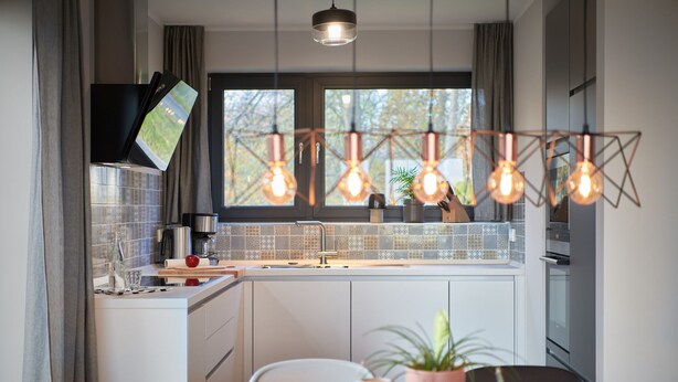 A modern kitchen with a large window, pendant lights, and a flat-screen TV mounted on the wall. - Welcome to Backsteinquartier B Putbus on the island of Rügen (Putbus)