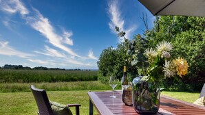 A wooden table with a glass of wine and a vase of flowers, set against a backdrop of a grassy field and trees under a clear sky. - Welcome to Backsteinquartier B Putbus on the island of Rügen (Putbus)