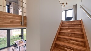 A modern interior with a wooden staircase, a dining area with a table and chairs, and large windows offering a view of the outdoors. - Welcome to Backsteinquartier B Putbus on the island of Rügen (Putbus)