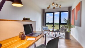 A modern room with a wooden desk, laptop, and lamp. There is a large window with a view of the outdoors. - Welcome to Backsteinquartier D in Putbus on Rügen (Putbus)