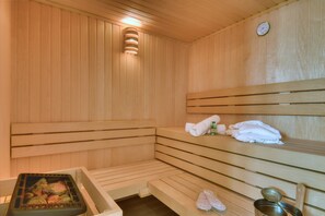 Un sauna en bois avec des bancs, un chauffage intégré dans un banc, des serviettes et une horloge au mur.