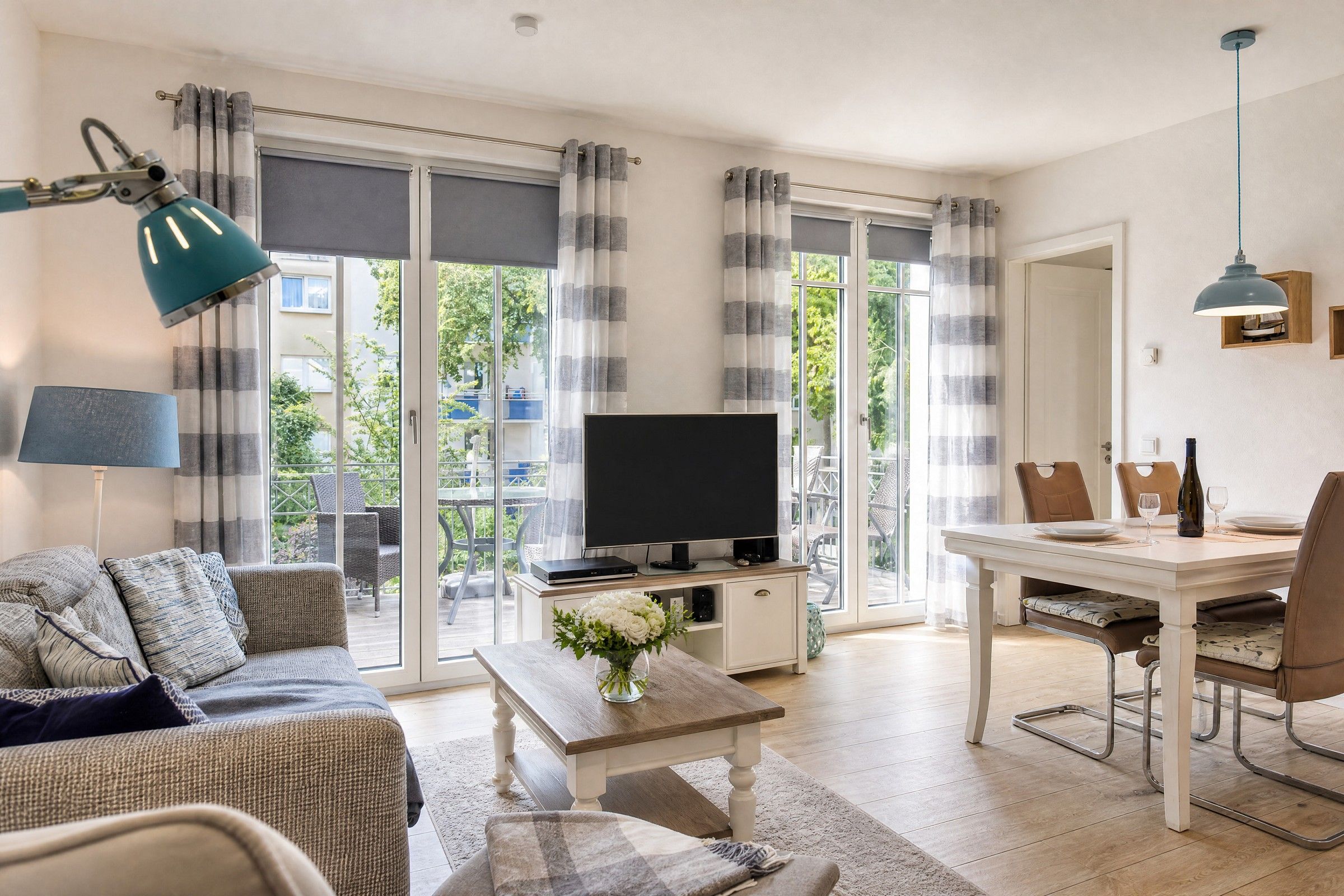 Una sala de estar con un sofá, una mesa de centro con un jarrón, un televisor y un comedor con sillas y una mesa.