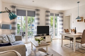A living room with a sofa, a coffee table with a vase, a TV, and a dining area with chairs and a table.