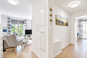 A modern living room with a flat-screen TV, a grey armchair, and a dining area with a white table.