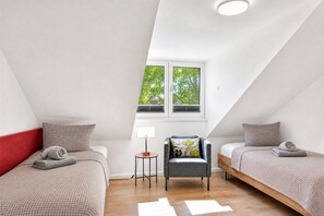 Un dormitorio con dos camas, una silla, una mesa y un ventanal con vistas a árboles.